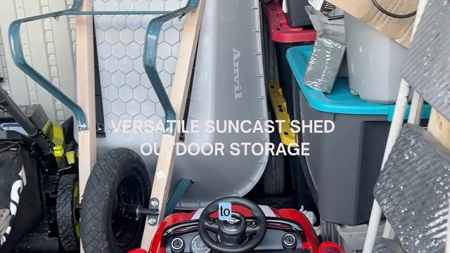 Inside a Suncast outdoor storage shed holding a lawn mower, wheelbarrow, storage bins and garden tools